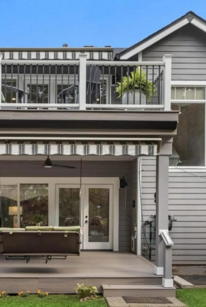 Backyard deck with glass doors, outdoor seating, and an upper balcony with a potted fern on the railing.